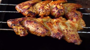 Delicious chicken wings on the skewers are frying and rotating above the fire