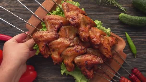Vista dall'alto di un piatto di legno pieno di deliziose ali di pollo fritto sugli spiedini — Video Stock
