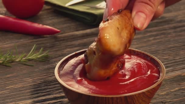 Primer plano de una mano sumergiendo un ala de pollo a la parrilla en el ketchup en un tazón — Vídeos de Stock