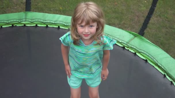 Een vrolijk meisje in een turquoise t-shirt springt op de trampoline — Stockvideo