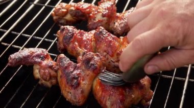 Erkek eller ızgaraya domates sosu ile lezzetli tavuk kanatları sürüyor.