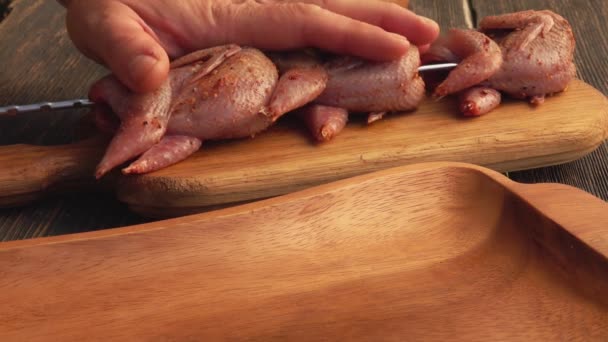 Primer plano de las manos masculinas perforando codornices crudas en los pinchos de la tabla de madera — Vídeos de Stock