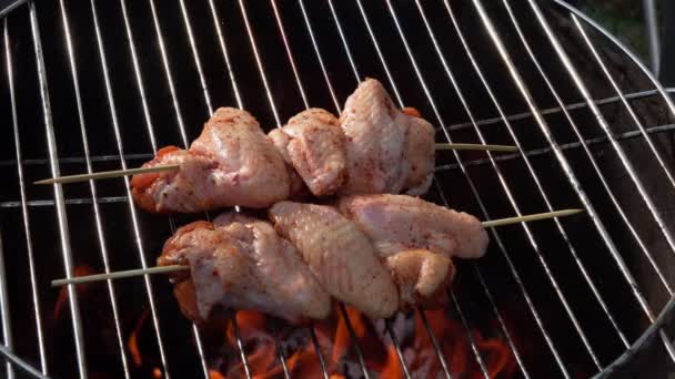 Las manos masculinas están colocando un pincho de madera con alas de pollo crudo en la rejilla de la parrilla — Vídeos de Stock