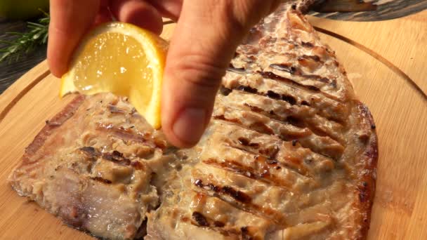 Hand kramar långsamt en citronsaft på den grillade vita makrillfiskfilén — Stockvideo