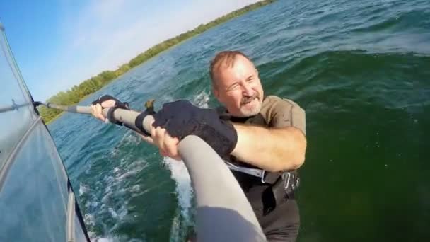 Barbudo hace vela en una tabla de windsurf en un hermoso lago — Vídeos de Stock