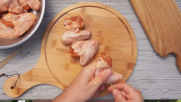 La vista dall'alto delle mani che perforano ali di pollo piccanti con uno spiedo di legno — Video Stock