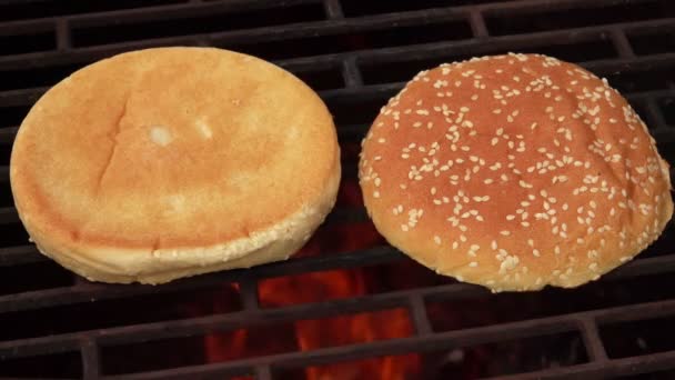 Close-up dari roti burger wijen yang digoreng pada kisi panggangan di atas api terbuka — Stok Video