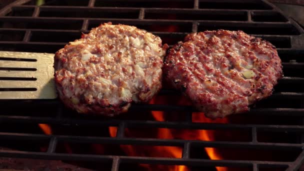 Primer plano de dos jugosas chuletas de hamburguesas de carne con cebollas volteadas con espátula — Vídeos de Stock