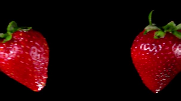 Strawberries collide and rotate on black background — Stock Video