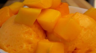 Taze mango küpleri donmuş mango dondurmasıyla dolu beyaz bir kaseye düşüyor.