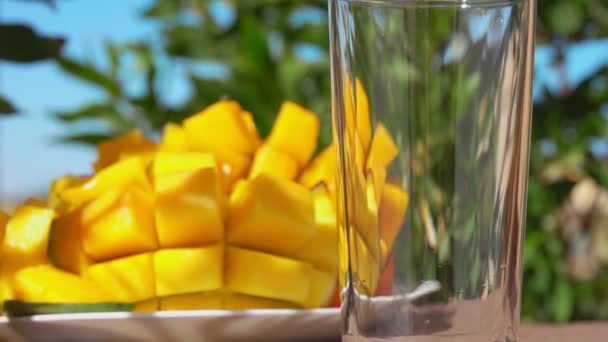 Świeży sok z mango jest wlewany do wysokiej szklanki obok dużego dojrzałego mango — Wideo stockowe