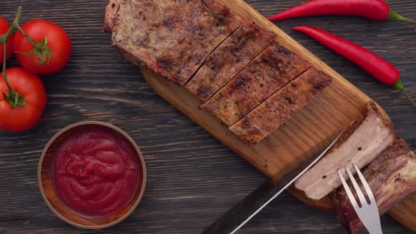 Vista dall'alto del coltello e della forchetta che tagliano le succose costole grigliate su un tavolo di legno — Video Stock