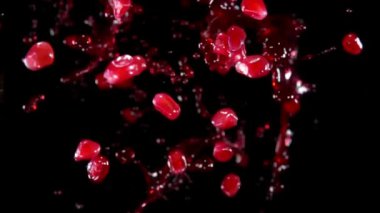 Olgun nar taneleri koyu bir arka planda meyve suyuyla uçuşuyor.