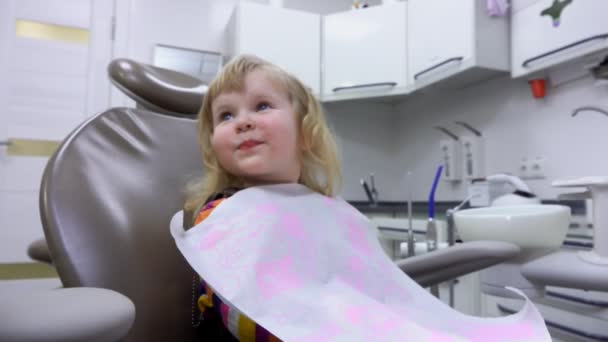 Маленький ребенок улыбается и открывает рот, чтобы стоматолог мог проверить его зубы — стоковое видео