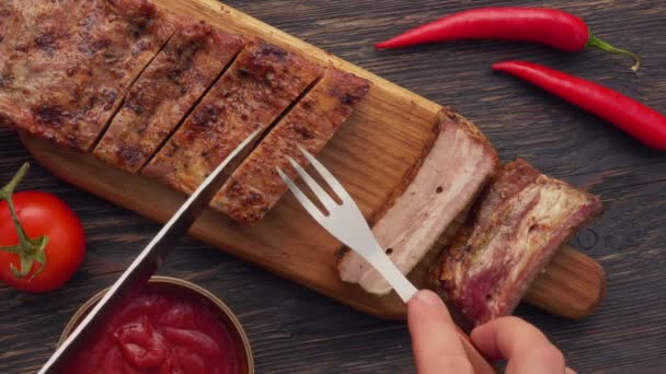 Bovenaanzicht van het mes en de vork die de sappige gegrilde ribben op een houten tafel controleren — Stockvideo