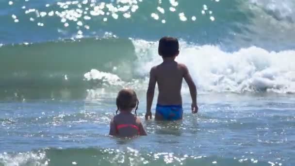 Rückansicht des Jungen und des Mädchens, die in plätschernde Meereswellen am Strand springen Stock-Filmmaterial