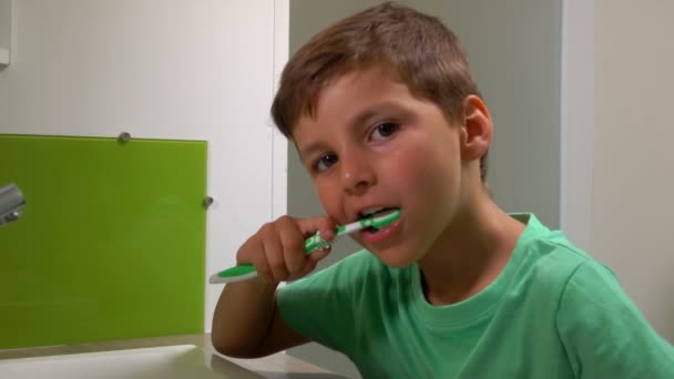 Mały wesoły chłopiec w zielonej koszulce myje zęby w łazience. — Wideo stockowe