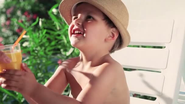 Jongen drinken sinaasappelsap. jongen in een hoed op het strand — Stockvideo