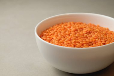 Canlı turuncu mercimeklerle dolu el değmemiş beyaz bir kase tarafsız bir zeminde duruyor. Mercimeğin pürüzsüz dokusu taze ve lezzetli bir yemeğe hazır olduğunu gösteriyor..