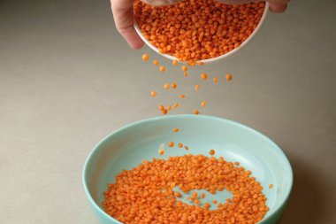 Parlak turuncu mercimek küçük bir kaseden daha büyük bir açık mavi tabağa geçer. Canlı renk, nötr mutfak zeminine karşı güzel bir tezat oluşturuyor, bir hazırlık anı sergiliyor.