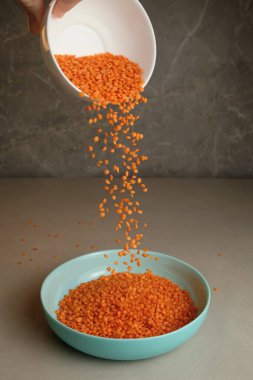 Parlak turuncu mercimek, beyaz bir kaseden sığ bir turkuaz tabağa dökülür. Mutfak ortamındaki taze malzemelerin güzelliğini vurgulayan renkli bir sahne yaratır..