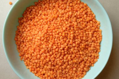 Parlak turuncu mercimeklerle dolu bir kase nötr bir yüzeyde duruyor ve pürüzsüz yuvarlak şekillerini sergiliyor. Bu mercimek yaratıcı yemek fikirlerine davetiye çıkarıyor, sağlıklı yemekler için mükemmel..