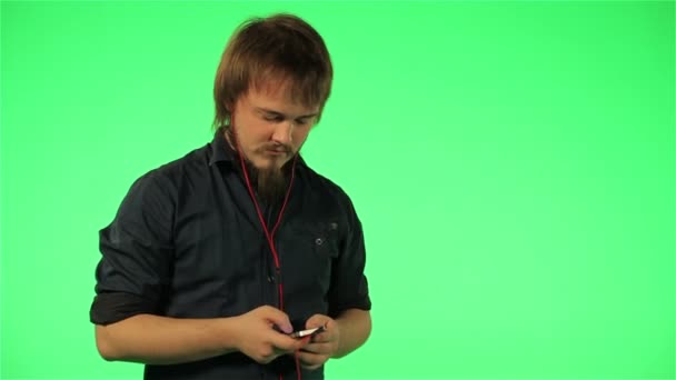 Человек слушает музыку по телефону на зеленом экране — стоковое видео