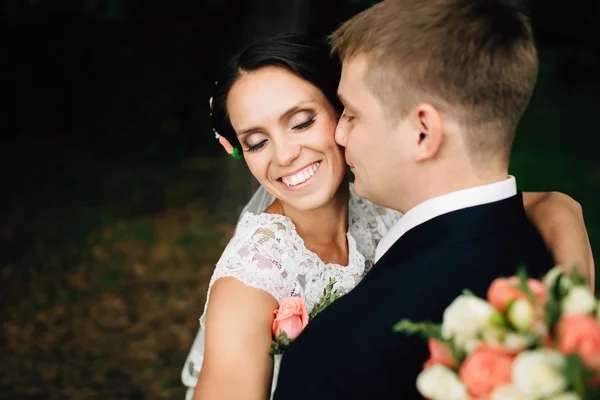 Elegant elegant brudgummen omfamnar med sin glad brud i park — Stockfoto