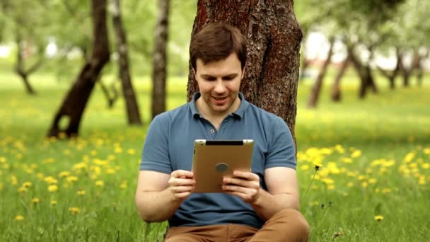 Piuttosto sorridente hipster uomo utilizzando il suo tablet pc in una giornata di sole — Video Stock