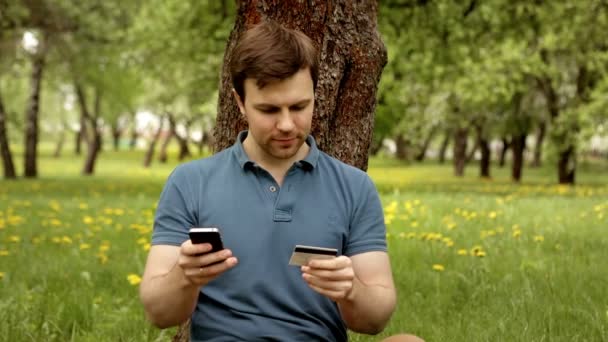 Bonito homem com cartão de crédito e telefone durante as compras através da internet — Vídeo de Stock