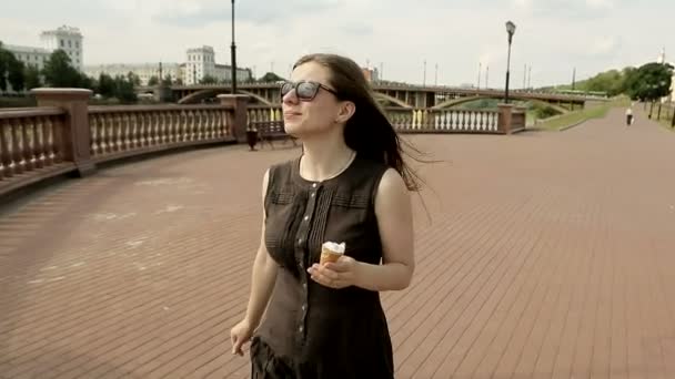 Привлекательная женщина в солнечных очках на улице ходит и ест мороженое — стоковое видео
