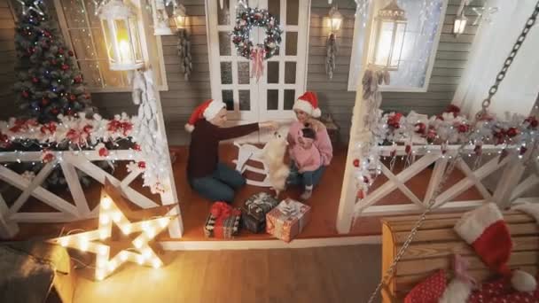 Jeune famille avec petite fille et chien assis sur le porche avec arbre de Noël — Video