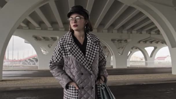 Hermosa modelo de moda. Mujer con estilo en abrigo de pie debajo del puente. — Vídeos de Stock