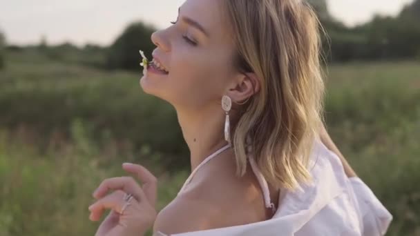 Junge Frau bei Sonnenuntergang mit Blume im Mund. Sommertag. Freiheitskonzept. — Stockvideo