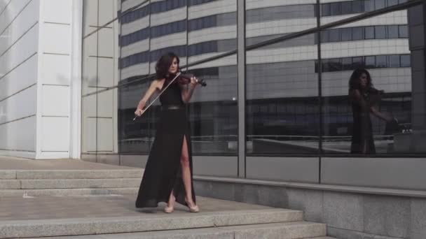 Mooie violist in zwarte jurk in de buurt van glazen gebouw. Stedelijk kunstconcept — Stockvideo