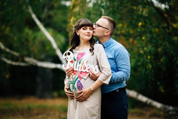 Embarazada mujer y su apuesto marido encantador abrazo en la naturaleza, hacer un picnic en el parque . — Foto de Stock