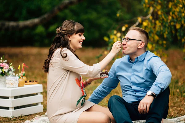 Joven hermosa embarazada hermosa alimenta a su marido guapo con pastel en el picnic . — Foto de Stock