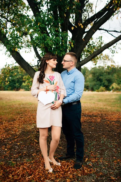 Esperando embarazada feliz pareja sosteniendo en blanco tablero de carbón en forma de corazón . — Foto de Stock