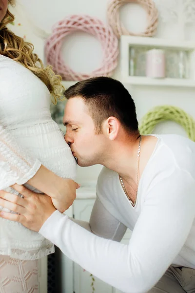 Feliz hombre besando vientre de su encantadora esposa embarazada de pie en el dormitorio . — Foto de Stock