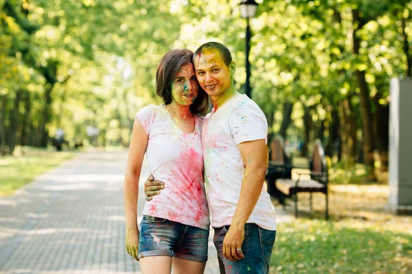 Ung och vacker, hipster par skrattar glatt åt kameran i parken på holi färg festival med färg färg pulver. — Stockfoto