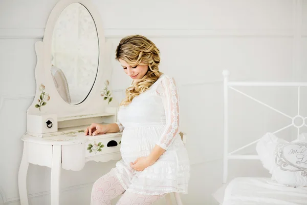 Jovem mulher grávida bonita em vestido branco sentado na cadeira . Imagens Royalty-Free