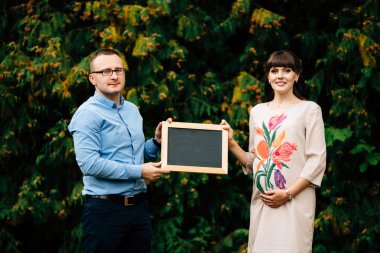 Expecting pregnant happy couple holding a blank charcoal board.