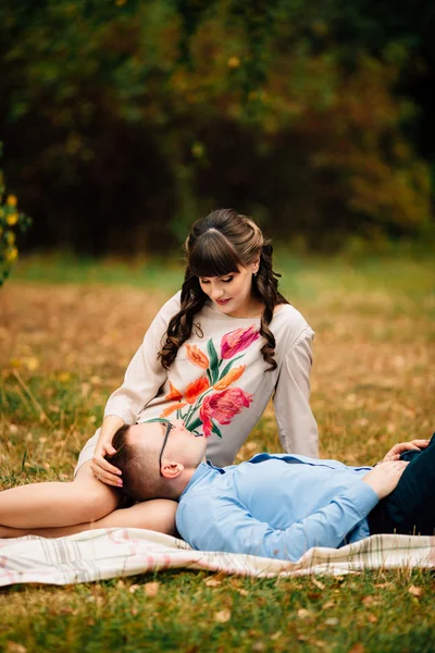 Handsome husband lying on his young pregnant beautiful woman's leg in park. — Stock Photo, Image