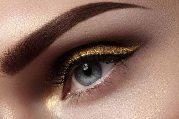 Hermoso macroplano de ojo femenino con maquillaje ceremonial. Forma perfecta de cejas, delineador de ojos y bonita línea de oro en el párpado. Cosméticos y maquillaje. Primer plano macro disparo de la moda sparcle visage — Foto de Stock