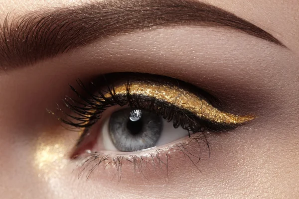 Hermoso macroplano de ojo femenino con maquillaje ceremonial. Forma perfecta de cejas, delineador de ojos y bonita línea de oro en el párpado. Cosméticos y maquillaje. Primer plano macro disparo de la moda sparcle visage — Foto de Stock