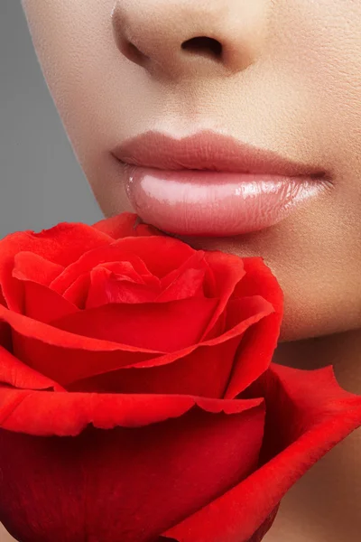 Close-up hermosos labios femeninos con maquillaje brillante brillo de labios. Piel limpia perfecta, maquillaje de labios fresco y ligero. Hermoso retrato de spa con tierna flor rosa. Spa y cosméticos — Foto de Stock