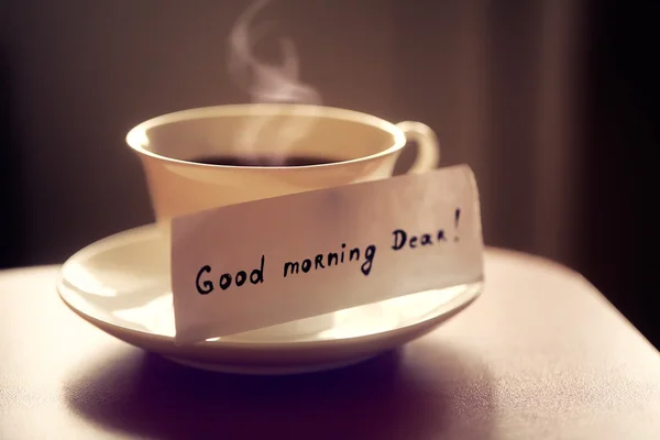 White ceramic cup of tea or coffee with nice letter 'good morning dear' on kitchen wood table. Beautiful photo with breakfast. — Stock Photo, Image