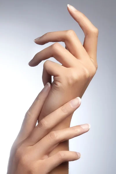 Belle braccia femminili con manicure francese ideale su sfondo grigio. Cura delle mani femminili, pelle morbida e sana. Spa & cosmetici. Cura della bellezza. Primo piano di belle dita famele con smalto per unghie — Foto Stock