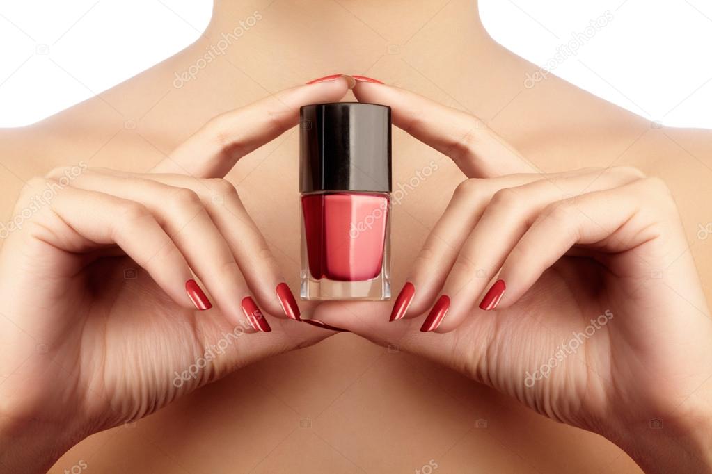 Beautiful female hands with perfect shiny red manicure holding nail polish lacquer. Care about female hands, healthy soft skin. Bright red nails
