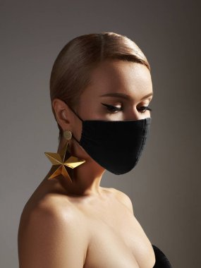 Yüzünde siyah ilaç maskesi olan güzel bir kadın. Moda makyajı, kutlama stili, altın takılar. Viral covid-19 salgınında hijyenli güzellik. Parti stili.